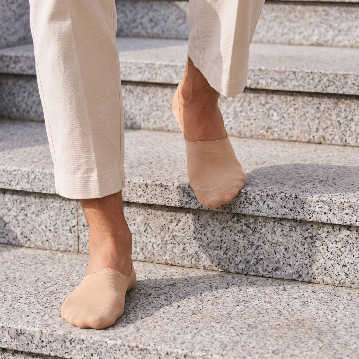 Nude no-show socks worn with cream trousers on stone steps